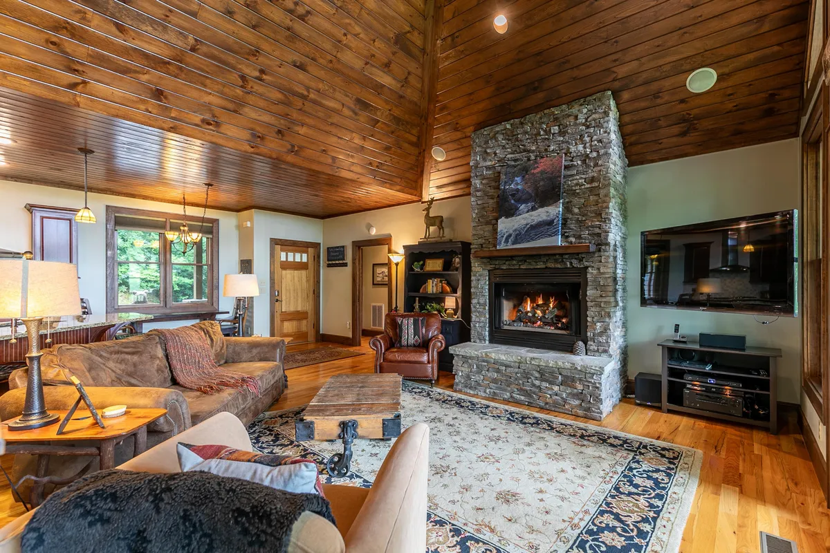 A cozy living area featuring a fireplace, wooden ceiling, soft rug, sofa, and coffee table—a classic setting for winter relaxation. The scene is warm and inviting, perfect for gathering with family for board games or watching snow fall outside.