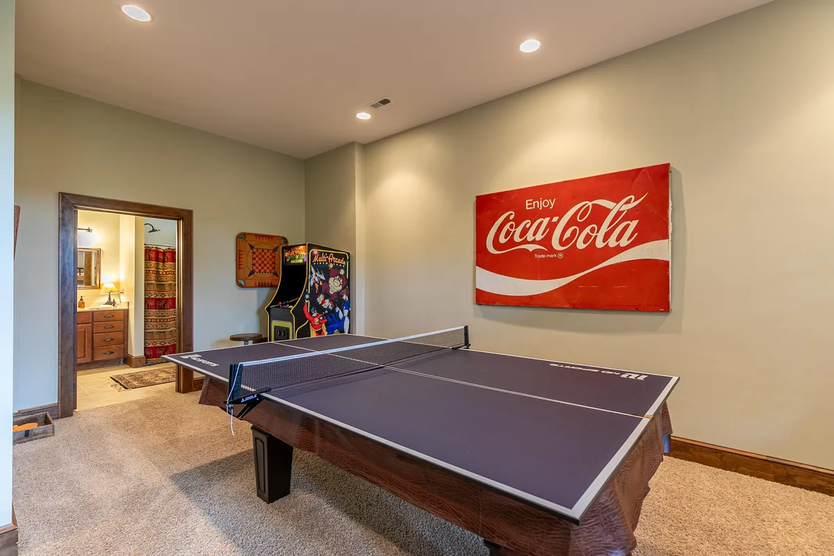 An energetic space focused on a ping pong table, a bright Coca-Cola wall sign, and an arcade machine. The atmosphere is playful, with plenty of space for friendly rivalry and laughter.