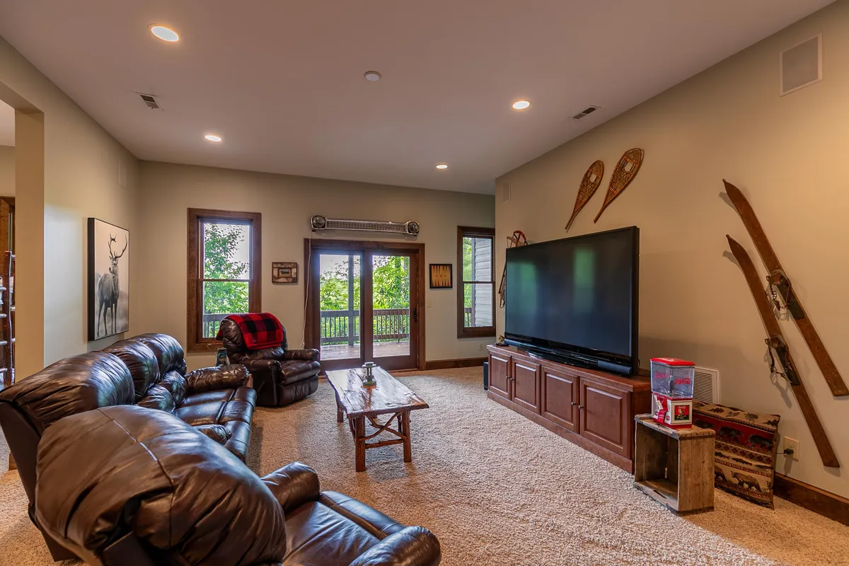 A cozy living space with reclining leather sofas, a large TV, wooden coffee table, and windows revealing outdoor views. The room is inviting, blending comfort for work breaks with a connection to the outdoors through visible natural light and views.
