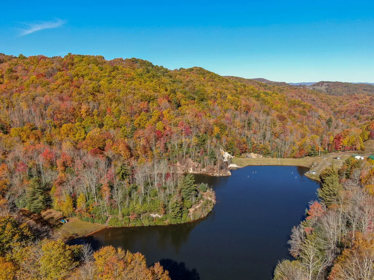 A peaceful lakeside scene with colorful autumn foliage framing the banks of a serene lake, set against distant mountains. In the foreground, people are seen fishing and picnicking by the water, encapsulating the area's natural beauty and recreational opportunities.