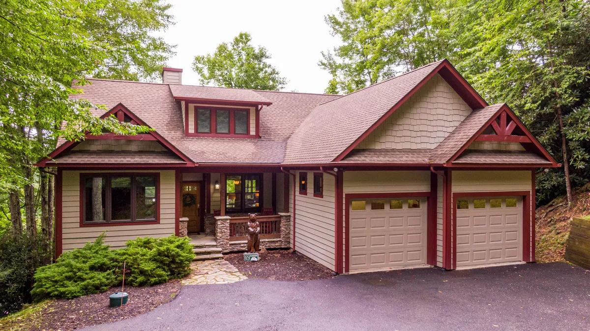 A welcoming front porch with comfortable seating and a stone pathway, framed by garage doors and windows. The setting invites guests for relaxed evenings or morning coffees while taking in the natural surroundings.