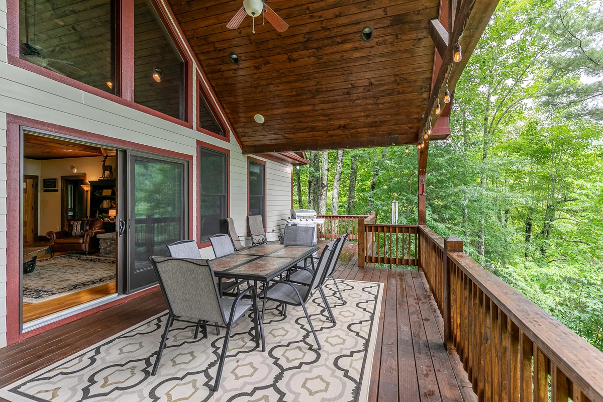 This image showcases a wooden deck set amidst lush greenery, featuring a dining table perfect for outdoor meals and gatherings. The tranquil setting hints at sunset views and the opportunity for al fresco dining and conversations with nature as a backdrop.