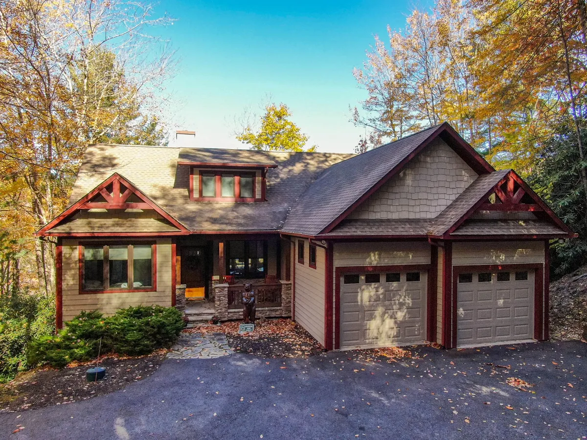 The inviting front porch of the home framed by wooden accents, dual garage doors, and a stone pathway, set against a backdrop of seasonal foliage. The exterior feels both welcoming and adventurous, suggesting a launch point for outdoor exploration or a return from the trails.
