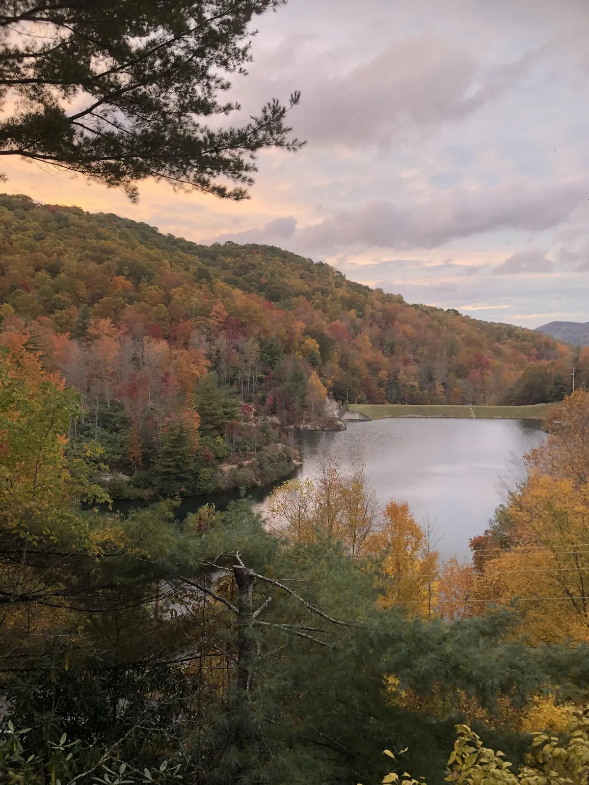 A serene view of colorful autumn foliage surrounding a calm lake, with distant hills providing a scenic backdrop. The vibrant leaves and peaceful water invite exploration and outdoor observation in the transitional seasons.