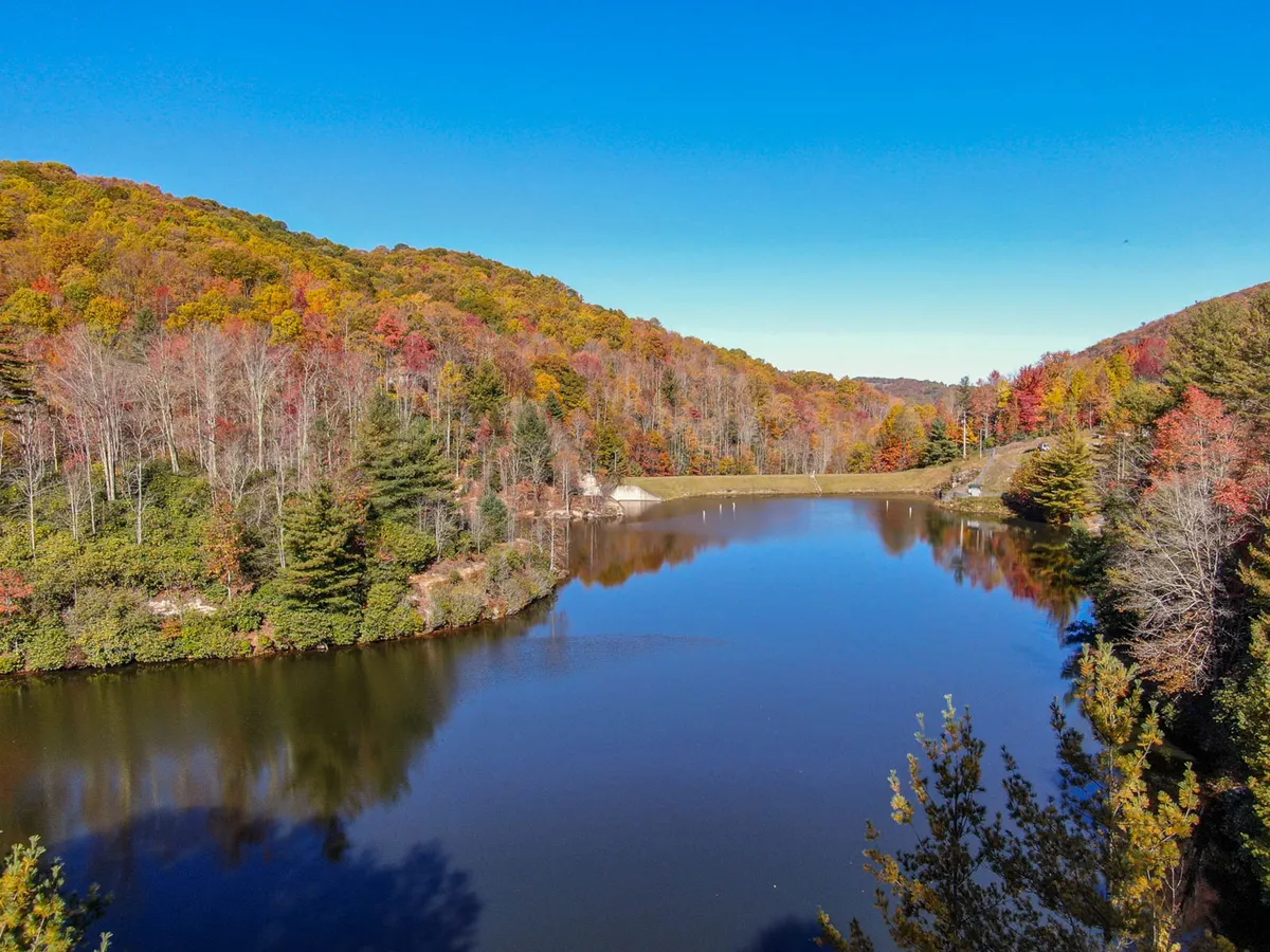 A stunning lakeside view captures autumn foliage, a calm lake, and distant mountains, evoking the serene natural beauty that surrounds Buckeye Lake. The vibrant colors and tranquil water reinforce the connection to the outdoors.