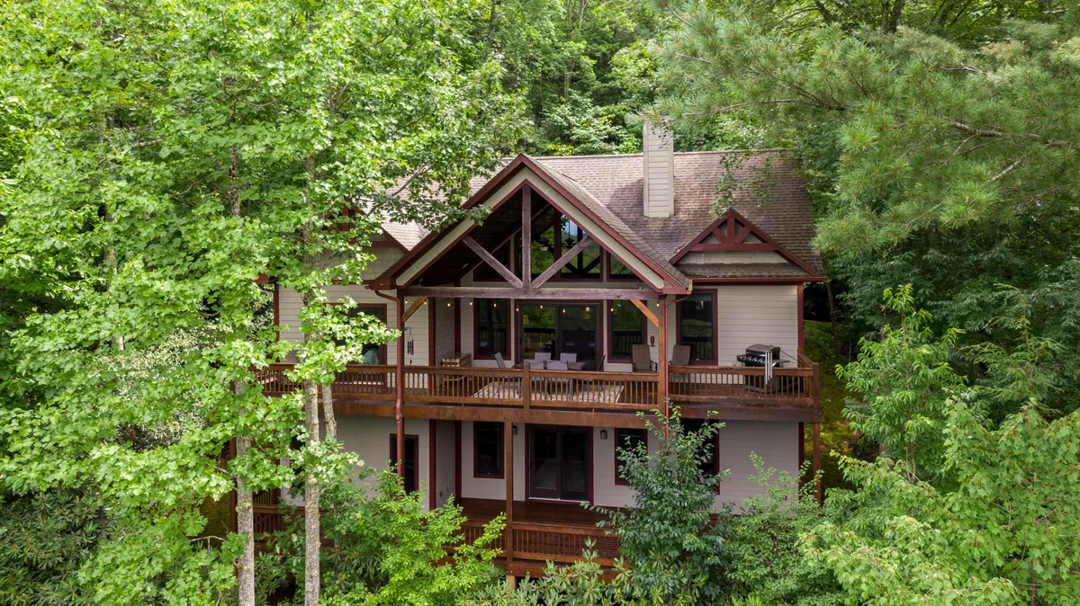 The image showcases the home's exterior nestled among lush trees, with a spacious balcony overlooking Buckeye Lake. Gentle sunlight bathes the house, inviting guests to unwind on the balcony and take in the serene, high-elevation views.