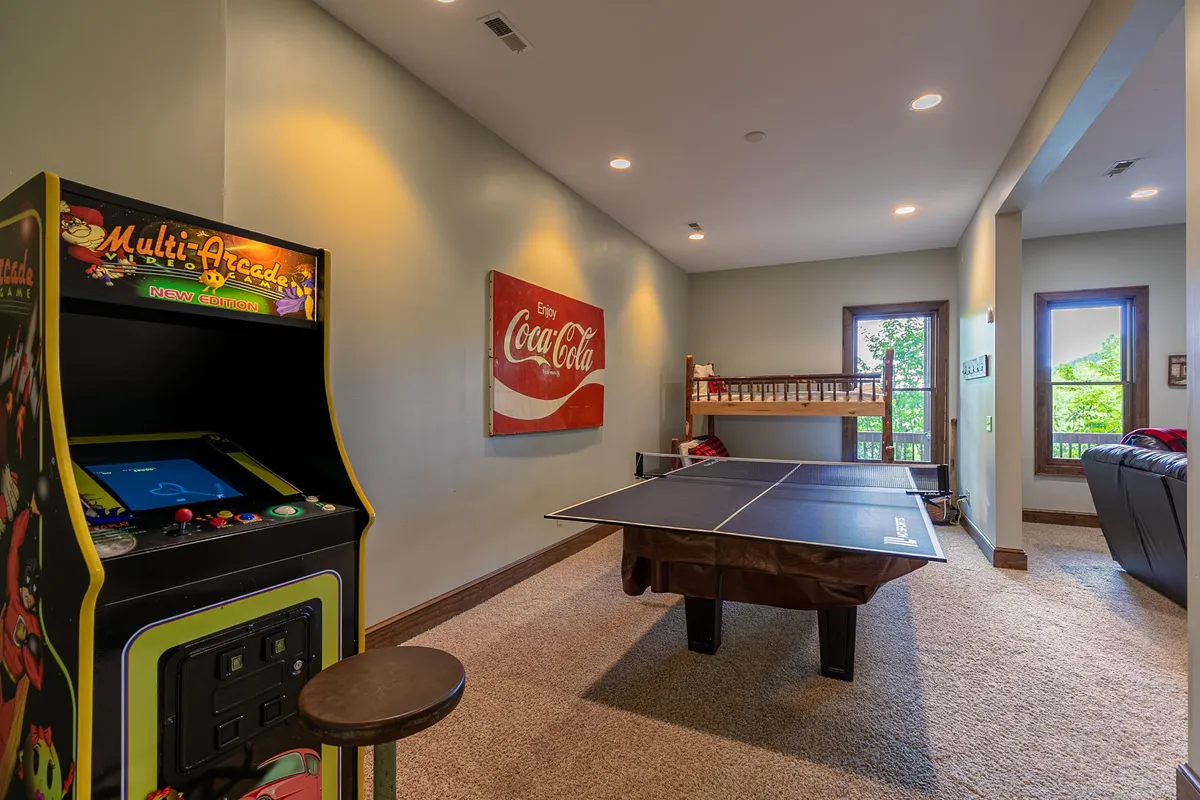 A vibrant game room featuring a classic arcade machine, a ping pong table, a prominent Coca-Cola sign, and a comfortable sofa. The space is designed for socializing and play, with inviting decor that encourages friendly competition and group gatherings.