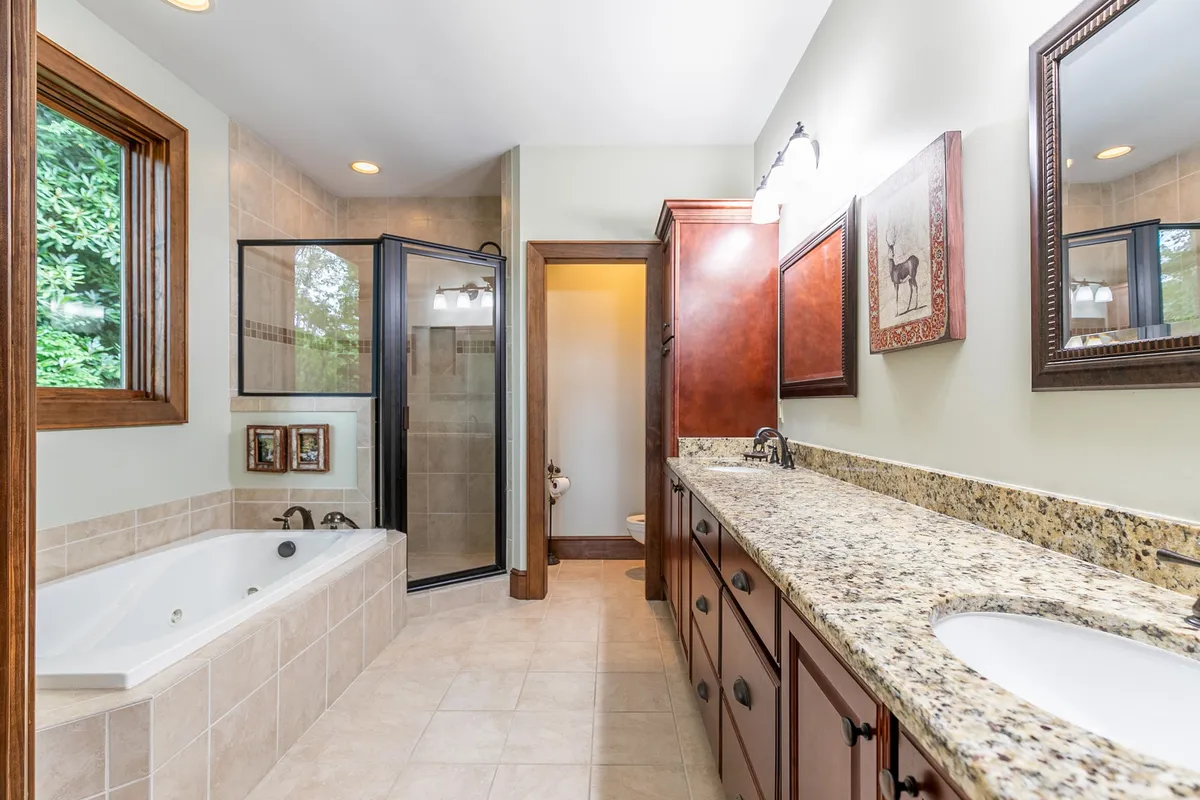 A luxurious bathroom with a granite-topped double vanity, a large soaking tub, shower enclosure, and elegant framed artwork, creating a spa-like atmosphere for unwinding and self-care.
