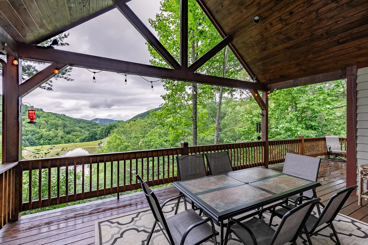 An inviting exterior dining area with a wooden table and chairs set beneath open beams, overlooking mountain views at sunset. Hanging lights and nature all around evoke a relaxed, social setting perfect for evening gatherings or morning coffee outdoors.